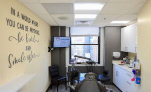 Modern Rittenhouse Smiles dental treatment room featuring a window with a Philadelphia skyline view and a wall quote reading In a world where you can be anything be kind and smile often.