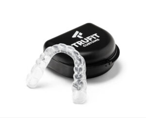 A clear plastic dental night guard resting in front of its open black carrying case featuring the TruFit Customs logo.