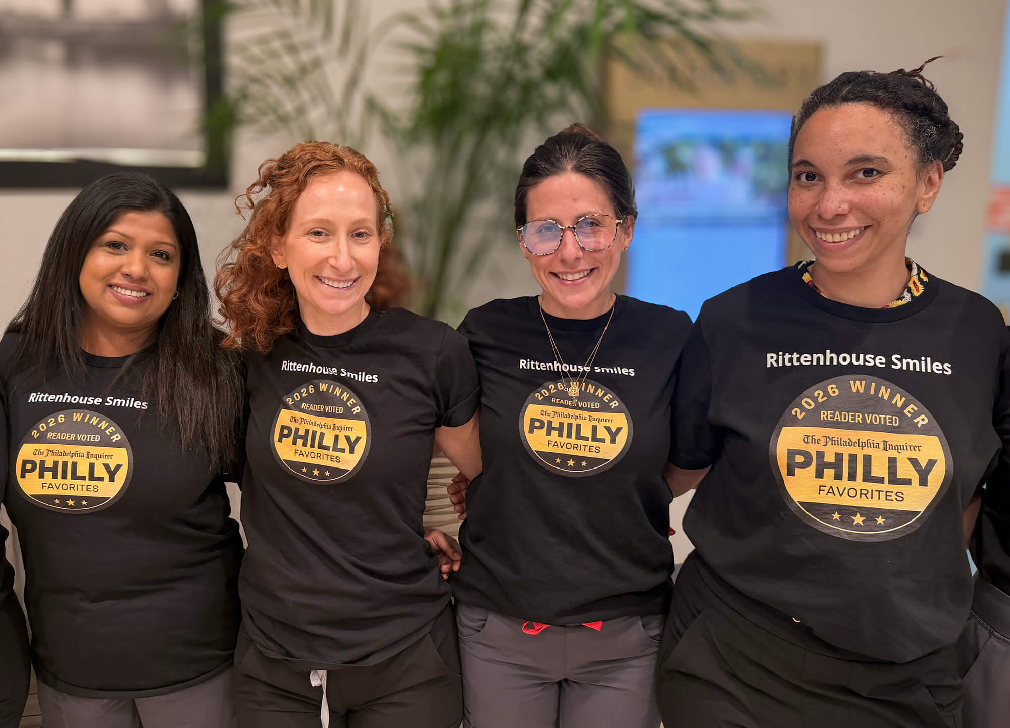 Four team members standing together and smiling, wearing matching black t-shirts that feature a gold seal reading "2026 Winner, Reader Voted, The Philadelphia Inquirer, Philly Favorites.