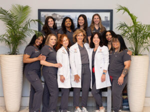 The Rittenhouse Smiles dental team smiling together in the lobby, featuring three doctors in white lab coats and seven team members in dark grey scrubs.