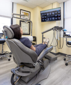 Patient relaxing in an ergonomic dental chair watching an overhead screen in a modern treatment room at Rittenhouse Smiles