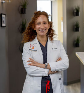 Dr. Kate Cooper standing in white lab coat with arms crossed smiling at Rittenhouse Smiles dental office
